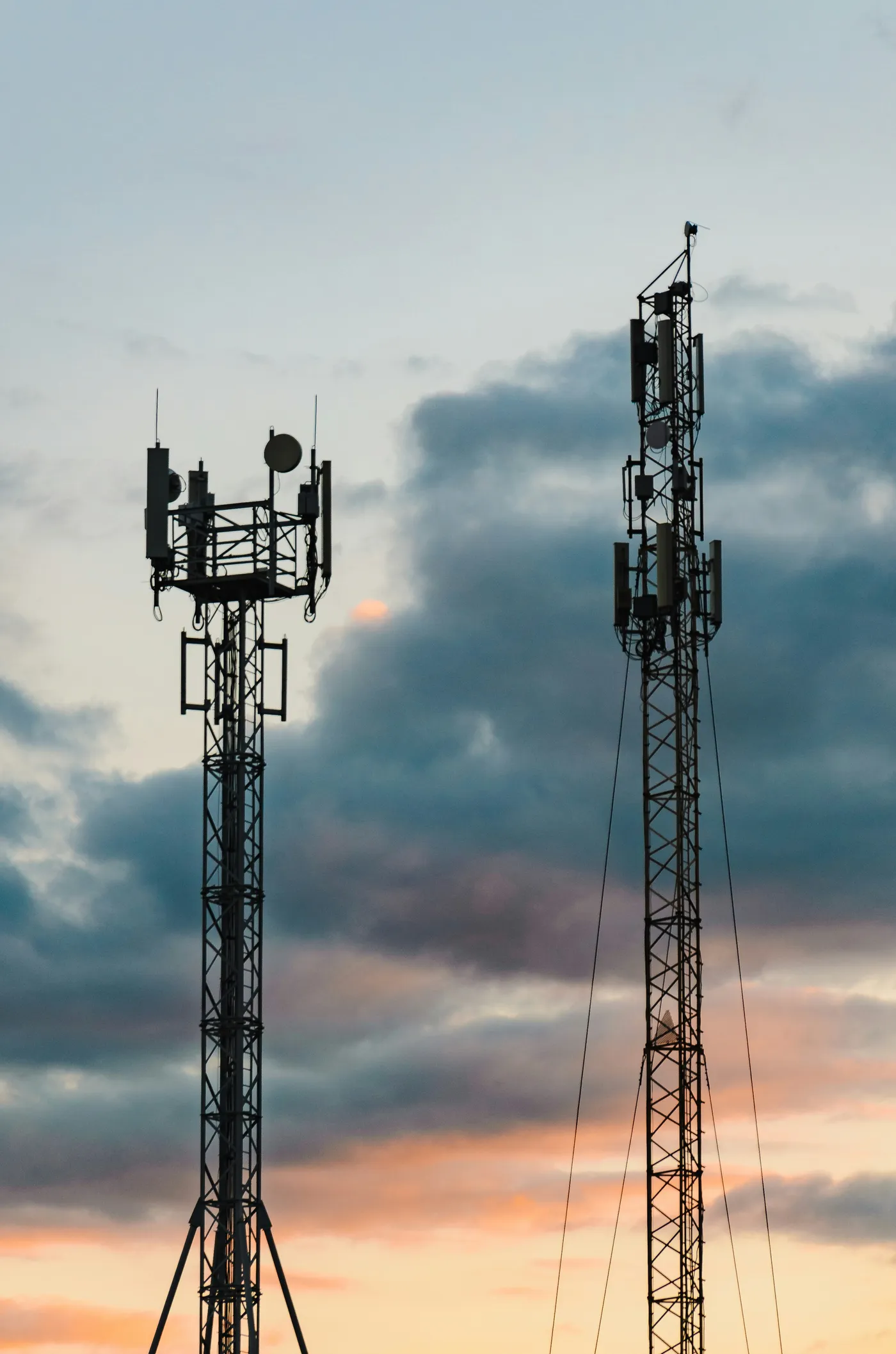 Two telecommunications towers silhouetted against a sunset sky